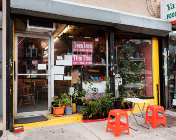 Photograph of the exterior with two stools and a table on the sidewalk.